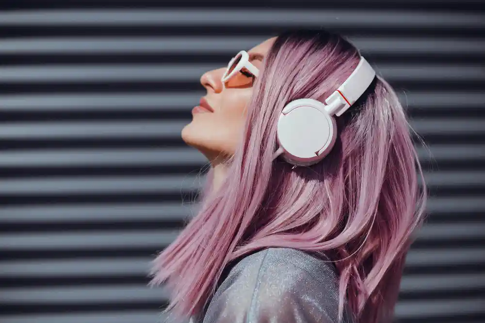 Woman with with pink hair wearing sunglasses and headphones outside