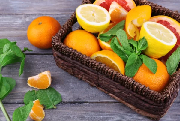 Fresh citrus fruits with green leaves in wicker basket on wooden background